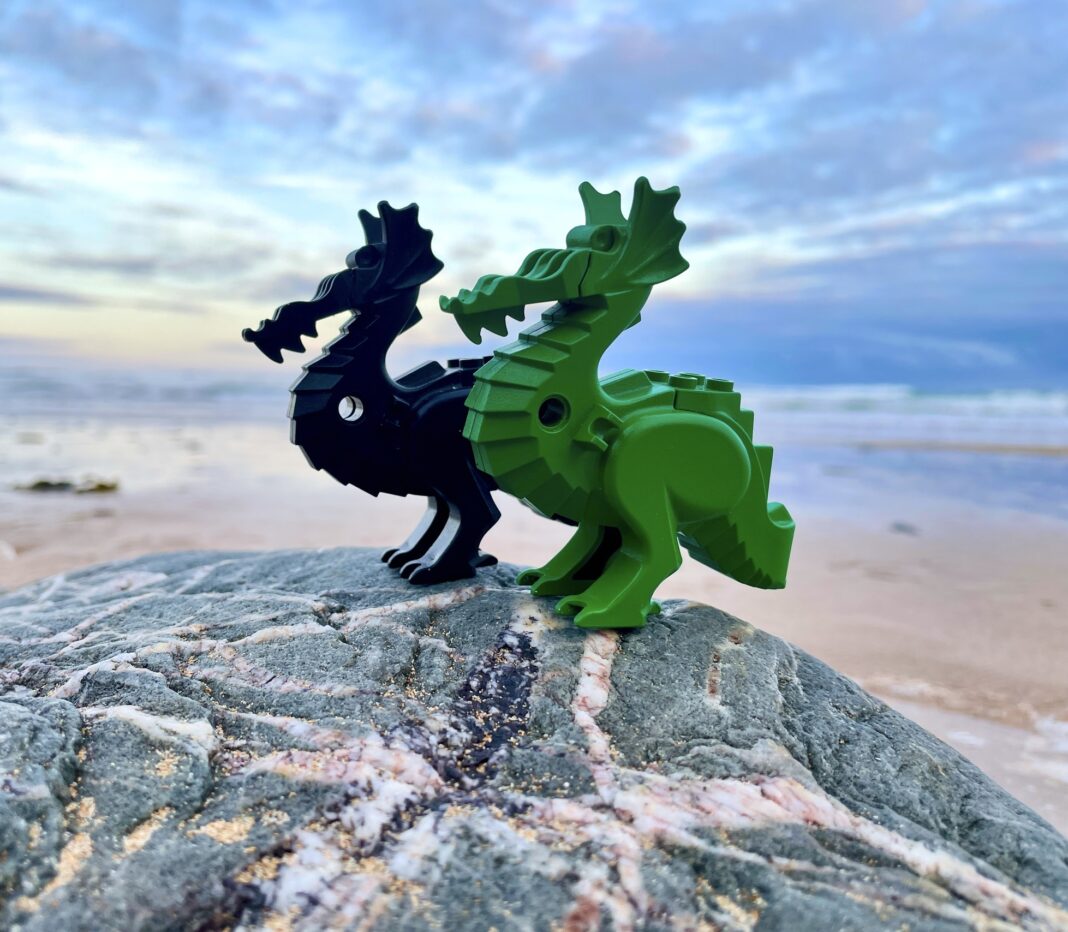 two lego dragons on a rock with ocean in background